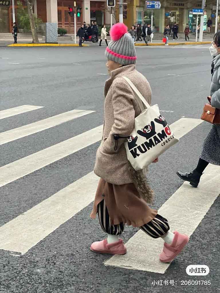 An elderly Chinese lady wearing a bright hat and carrying a fashionable bag