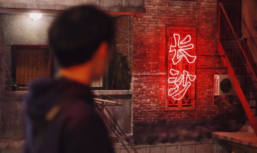 A man looking at a neon light with Chinese characters